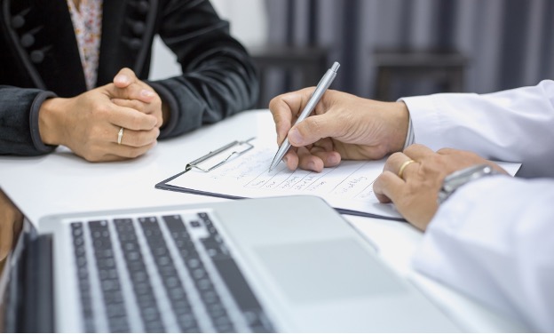 Male doctor taking notes while sitting with female patient