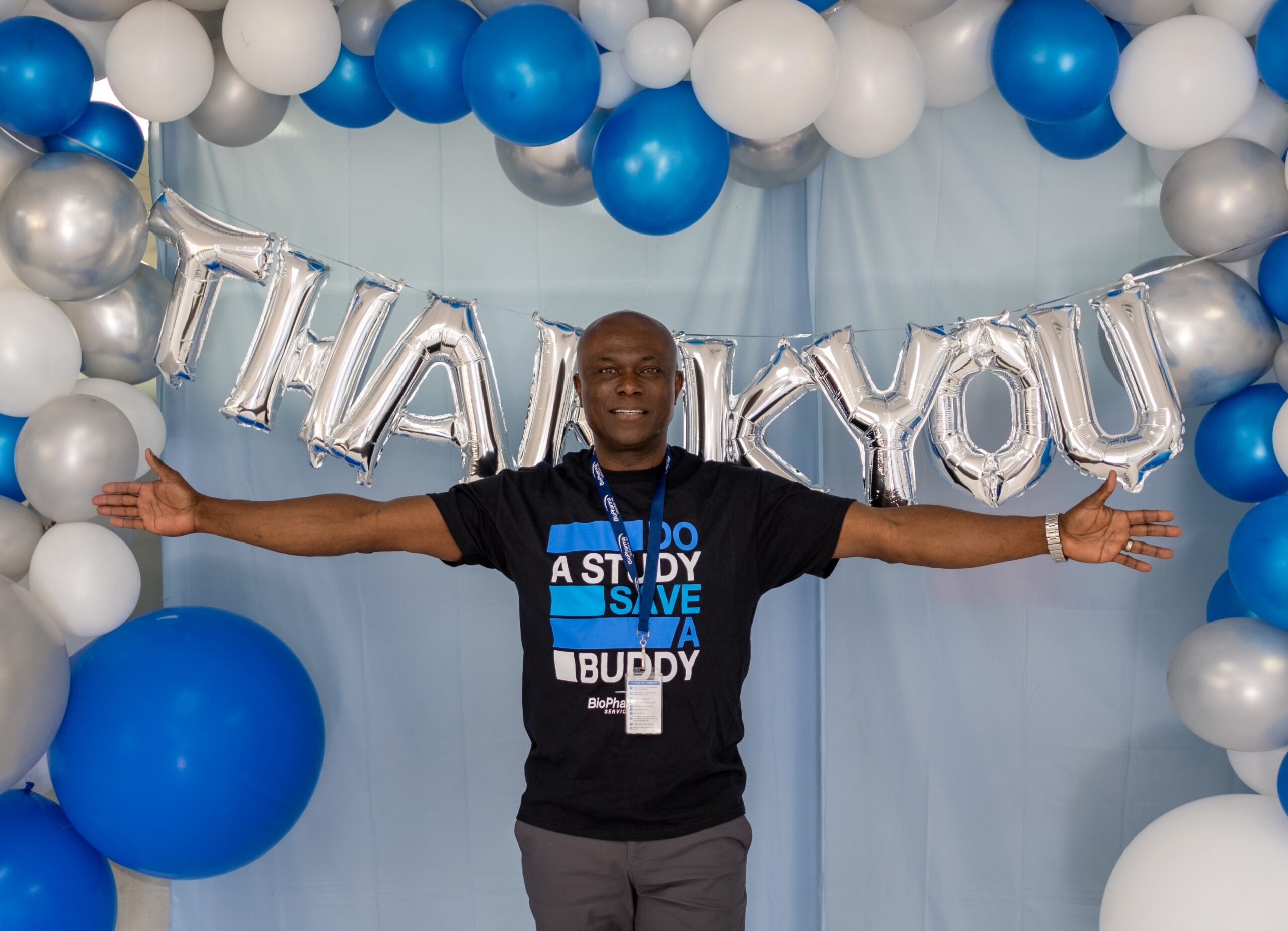 Person with open arms in front of a "Thank You" sign made of balloons