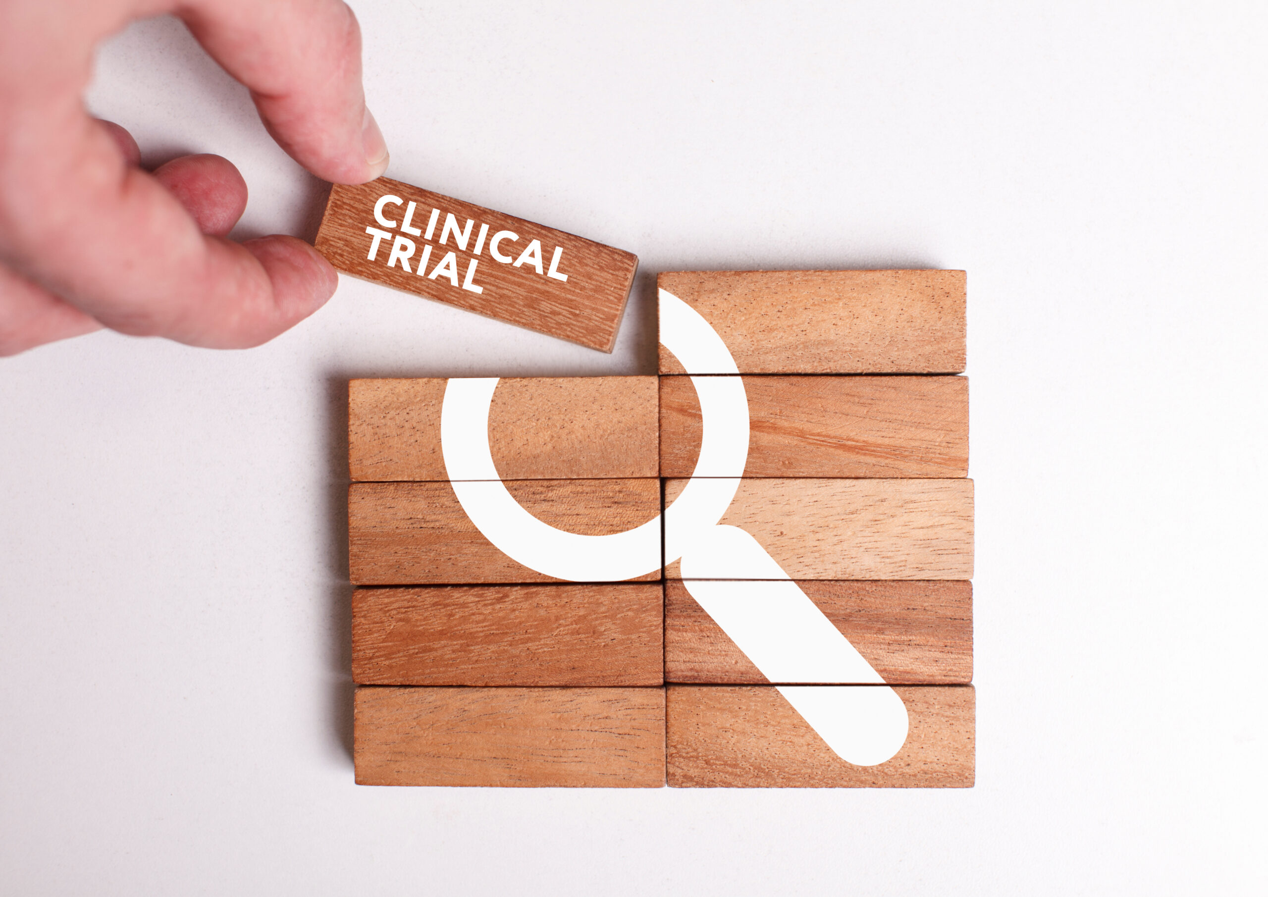 Hand stacks small pieces of wood, forming a magnifying glass, and the words "clinical trial."